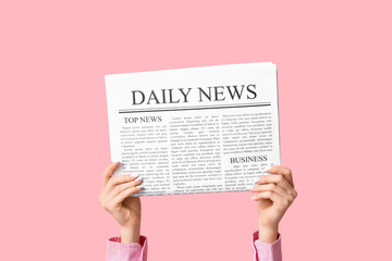 Female hands with newspaper on pink background
