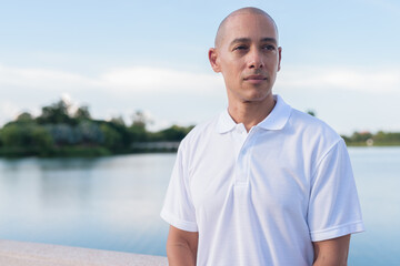 Confident bald man in white polo shirt posing by lake in serene outdoor portrait
