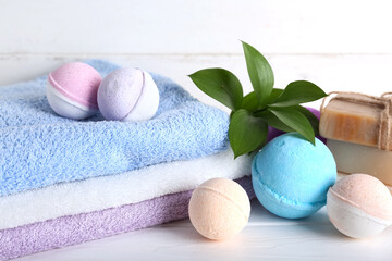 Bath bombs with towels and plant on white wooden table, closeup