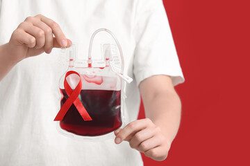 Woman with pack for transfusion and red ribbon on color background, closeup. Blood Cancer Awareness...
