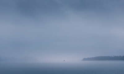Silhouette of fishing boat floating on Mondsee lake in misty fog. Minimalism Austria landscape background