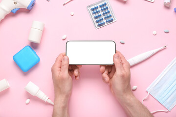 Male hands with blank mobile phone and medical supplies on pink background