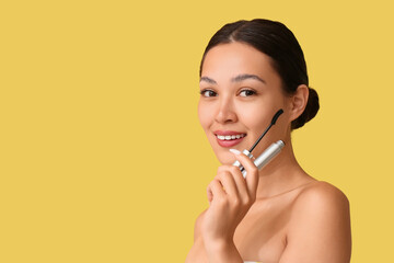 Happy young Asian woman with mascara on yellow background