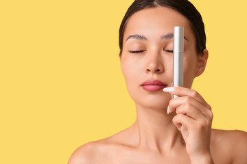 Beautiful young Asian woman with mascara on yellow background
