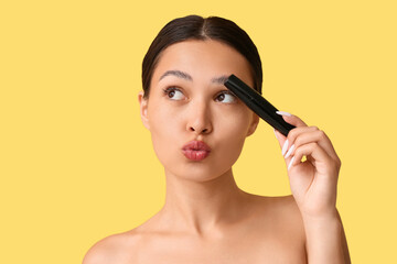 Fototapeta premium Beautiful young Asian woman with mascara blowing kiss on yellow background