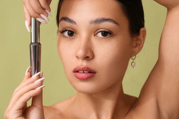 Beautiful young Asian woman with mascara on green background, closeup