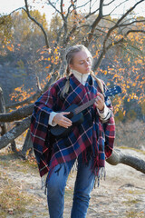 Portrait of smiling caucasian girl plays ukulele in autumnal park. Young woman plays guitar musical...