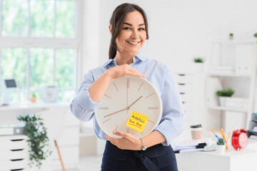 Businesswoman holding clock with text MANAGE YOUR TIME in office