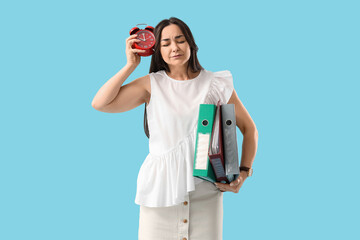 Stressed businesswoman with alarm clock and folders on blue background. Time management concept