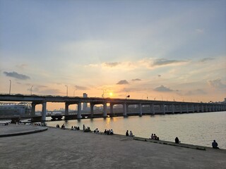 Young people sitting near the Double deck bridge by the floating island Sevit at sunset on Han River in downtown district Seoul, South Korea	 
