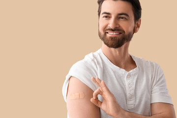 Young man with applied medical patch showing OK after vaccination on beige background, closeup