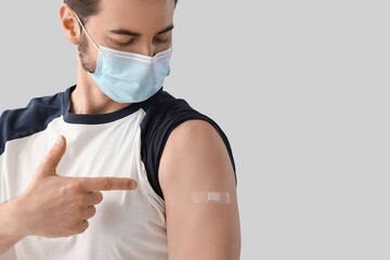 Young man in medical mask pointing at applied patch after vaccination on light background