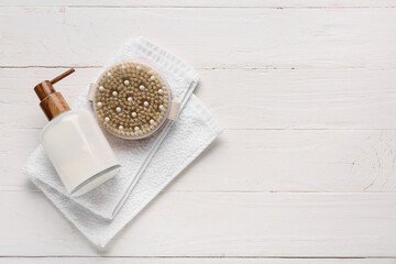 Composition with massage body brush, towel and bottle of cosmetic product on white wooden...