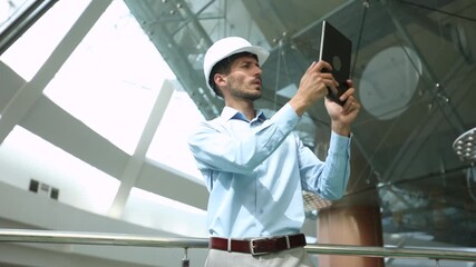 Handsome male architect making a note in digital tablet while looking up at construction site in building under construction - Powered by Adobe