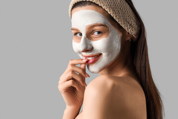 Beautiful young happy woman with clay mask on grey background