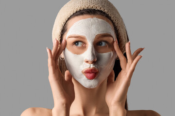 Beautiful young thoughtful woman with clay mask blowing kiss on grey background