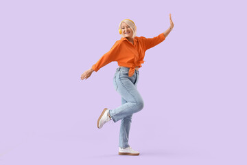 Beautiful mature woman in headphones dancing on color background