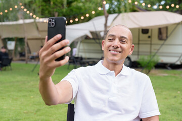 Happy man at campsite with camper van using phone while taking photo or having video call
