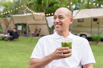 Confident bald man relaxing at campsite with camper van having healthy green detox juice drink