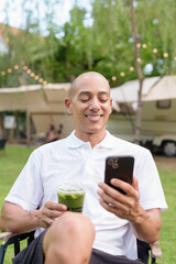 Bald man at campsite with camper van having healthy green detox juice drink and using phone