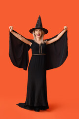 Beautiful happy mature woman dressed as witch on orange background. Halloween celebration