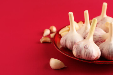 Plate with fresh garlics on red background