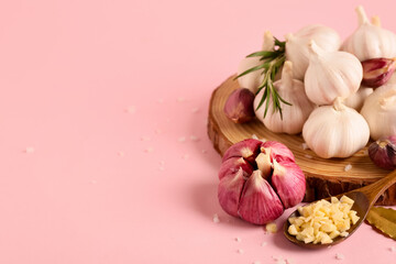 Wooden board with fresh garlics, rosemary and bay leaf on pink background