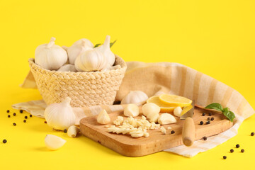 Wicker basket with fresh garlics, basil leaves and slices of lemon on yellow background