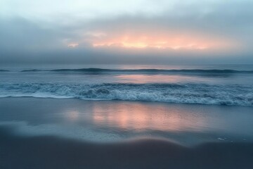 Obraz premium Calm ocean waves gently rolling onto the sandy shore under a cloudy sky with soft morning sunlight glowing on the horizon and reflecting on wet sand