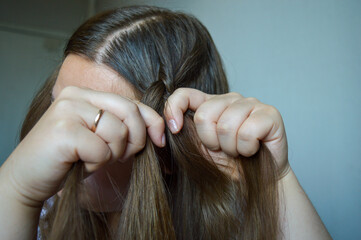 woman braiding her long hair, focusing on hands and strands. themes: beauty routine, hair care,...
