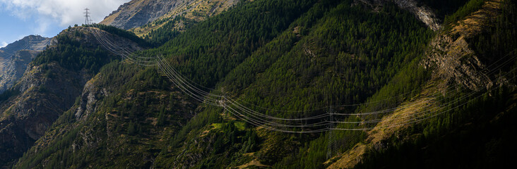 High-power power-line installed in the mountains, with electric cables illuminated by the sun,...