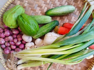 A bamboo winnowing basket contains various kinds of vegetables, including chayote, cucumber, shallots, garlic, leeks, carrots, and Chinese cabbage.
