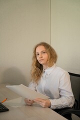Girl sit in office in white blouse with paper and looking to you