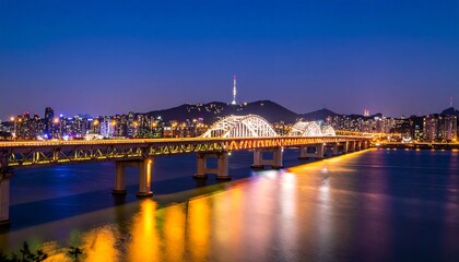 Obraz premium Illuminated bridge over a river at night, with city skyline in the background.