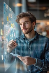 young man thoughtfully analyzing sticky notes and writing on glass wall in modern office environment