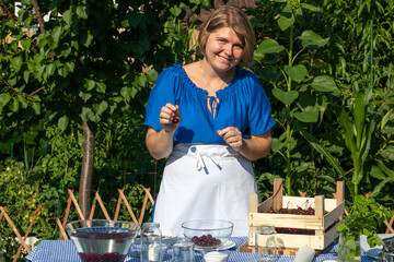 Smiling Caucasian woman in blue dress prepares sour cherry jam, evoking National Pickling Week and...