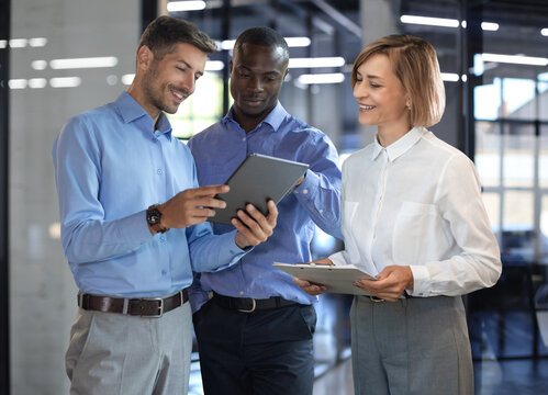 Three diverse business partners standing and discussing project working together at workspace.