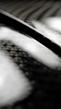 Extreme close-up macro video of abstract, pristine, high-tech dark metallic surface, polished black carbon fiber reflecting studio light, revealing a delicate curve, emphasizing advanced materiality