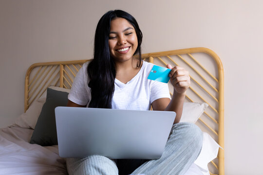 Smiling young woman using laptop and credit card on bed for online shopping - Powered by Adobe