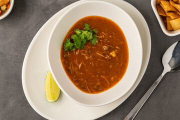 Spicy Mexican chicken soup with noodles, garnished with fresh cilantro and lime wedge