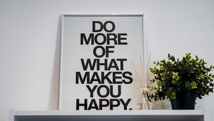 Framed motivational print with plant and diffuser on white shelf against a white background wall...