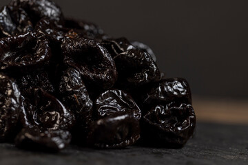 black sweet prunes made from small plums, piled on a board made of black stone dried plum fruits,...