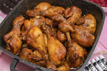 Juicy, golden-brown chicken drumsticks cooked in a rich savory sauce, served in a large black speckled roasting pan for a hearty meal.