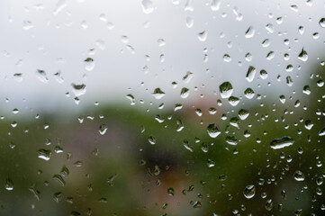 Close-up of raindrops on a window with a blurred outdoor background, capturing the droplets on the glass surface.