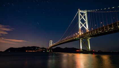 Fototapeta premium Illuminated suspension bridge at night over calm water.