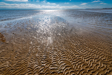 Menschenleere Nordseeküste mit ansteigendem Meerwasser bei Flut und glitzernder Wasseroberfläche im Gegenlicht der Sonne