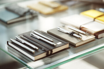 Silver Pens Lying on Black Notebooks on Glass Shelf writing stationery