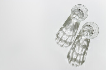 Two Transparent Water Glasses with dark shadows at sunlight on white, pastel color photo minimal...