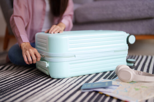 Adult Asian female prepares travel suitcase home floor holiday trip essentials map passport headphones journey vacation adventure