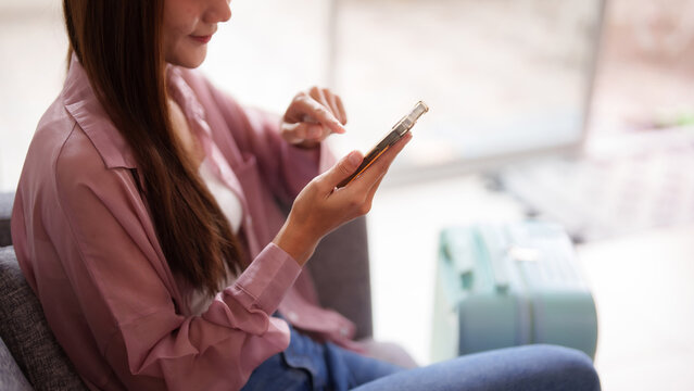 Asian adult woman traveler checks mobile phone content plans journey prepares departure comfortable airport lounge environment